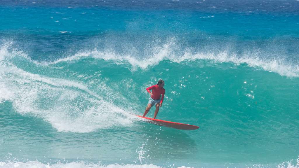 Surfer riding a turquoise wave on a longboard at Freights Bay, Barbados